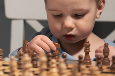 Genç zihin satranç tahtasını dikkatle inceler, stratejik dehanın bazen bebek bezleri, merak ve sevimli konsantrasyon yüzüyle geldiğini kanıtlayan.