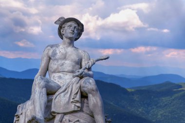 Yunan tanrısı ve habercisi Hermes 'in antik taş heykeli dramatik dağ manzarası ve bulutlu gökyüzüne oturmuş mitoloji, seyahat, iletişim, klasik sanat, tarih ve zamansız kültürü sembolize ediyor..
