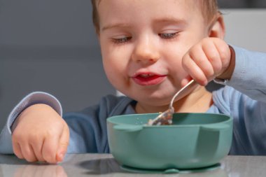 Çocuk kaşıkla bebek lapası yerken bağımsızlığı öğreniyor.