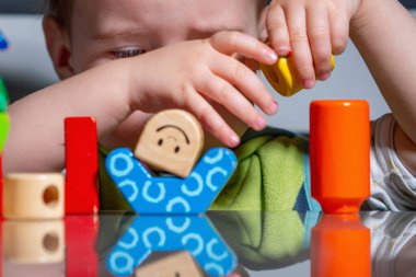 Küçük çocuk, merak ve sabırla ahşap blokları istifleyerek eğitici bir oyun oynuyor.