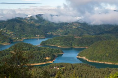 Zaovinsko Gölü, Tara Ulusal Parkı, Sırbistan 'da fırtına ve yaz sonu gün batımı sonrasında alçak bulutlarda dağ gölü