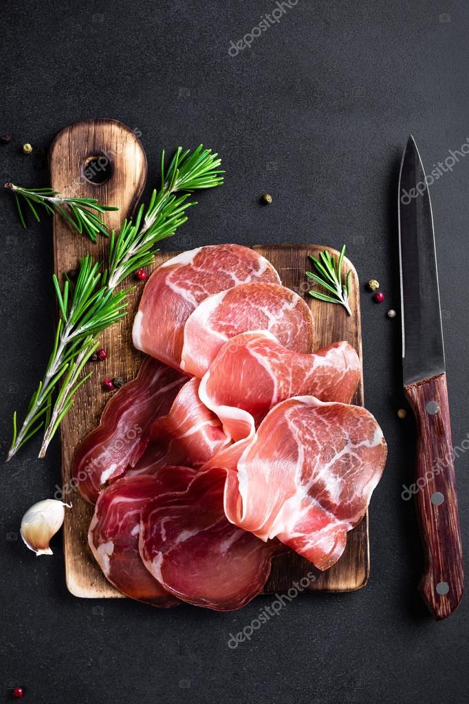 Prosciutto ham on dark background Stock Photo by ©yelenayemchuk 100261676