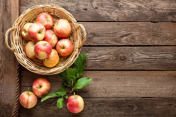 Verse rode appels in rieten mand op houten tafel. — Stockfoto