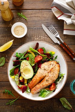 Izgara somon balığı bifteği, avokado ve domatesli taze sebze salatası, dolmalık biber ve yapraklı sebze. Üst görünüm