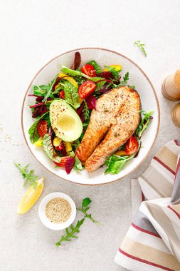 Izgara somon balığı bifteği, avokado ve domatesli taze sebze salatası, dolmalık biber ve yapraklı sebze. Üst görünüm