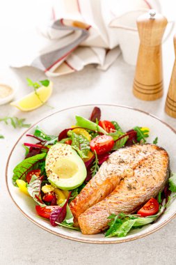 Izgara somon balığı bifteği, avokado ve domatesli taze sebze salatası, dolmalık biber ve yapraklı sebze.