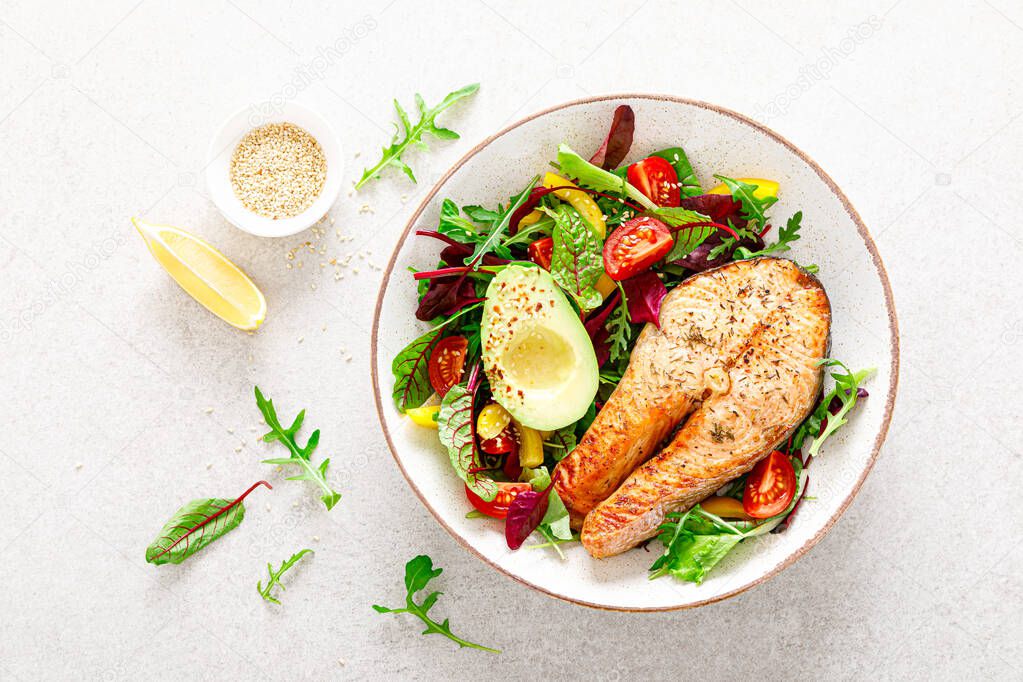 Salmon fish steak grilled, avocado and fresh vegetable salad with tomato, bell pepper and leafy vegetables