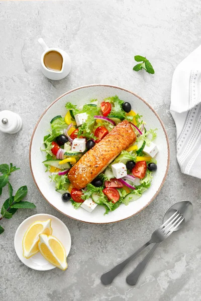 Salmon fish salad. Fresh vegetable greek salad with tomato, pepper, lettuce, olives, cucumbers, feta cheese and grilled salmon fish fillet in bowl, healthy food, omega 3, keto diet, mediterranean cusine, top view.