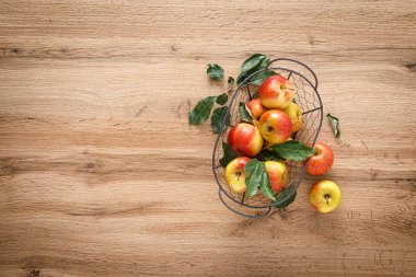 Tahta masa manzarasında yaprakları olan taze kırmızı elmalar.
