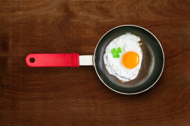 Kırmızı plastik saplı, küçük, boş, siyah tava. Kızarmış tavuk yumurtası, kahverengi doğal ahşap masa üzerinde çırpılmış yumurta.