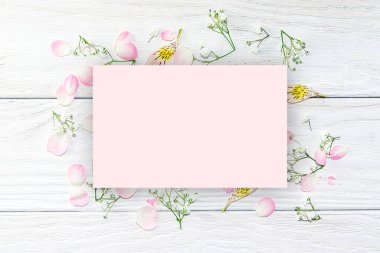 Hafif ahşap arka planda pembe gül yaprakları ve küçük beyaz çiçekler deseni. Güzel yaz, bahar, kartpostallar ve tasarım için arka plan..