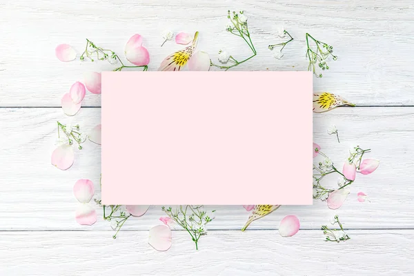 A pattern of pink rose petals and small white flowers on a light wooden background. Beautiful summer, spring mock up background for postcards, design.