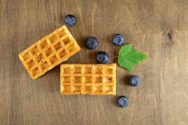Kahverengi ahşap bir masanın arka planında yabanmersinli yumuşak Belçika waffle 'ları, doğal desenli, üst görüşlü, uzay kopyası.