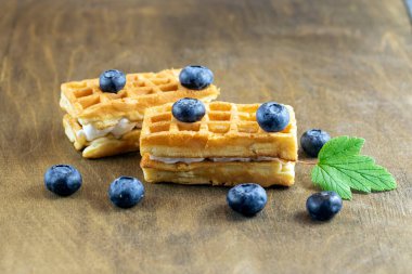 Kahverengi ahşap bir masanın arka planında yabanmersinli yumuşak Belçika waffle 'ları, doğal desenli, üst görüşlü, uzay kopyası.