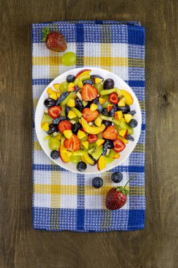 Üzüm, nektarin, kivi, çilek, böğürtlen, siyah ahşap zemin üzerinde hanımeli olan beyaz bir tabakta salata.