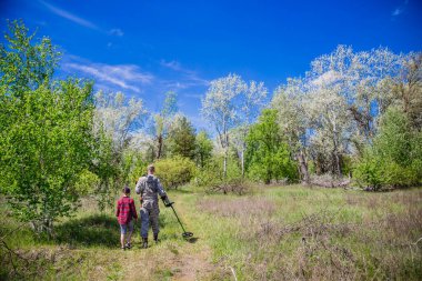 Elektronik metal dedektörlü hazine avcısı çocuğuyla hazine arıyor.
