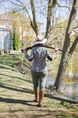 Zarif avcı kıyafetleri içinde kadın avcı avlanmaya hazır, bir silah tutuyor ve avını bekliyor.