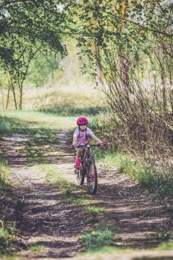 Little girl riding a bicycle in helmet in countryside