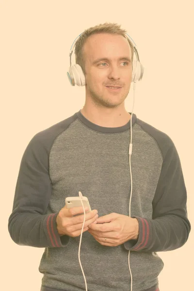 Onnellinen komea valkoihoinen mies kuuntelee musiikkia ja pitää matkapuhelin miettiessään — kuvapankkivalokuva