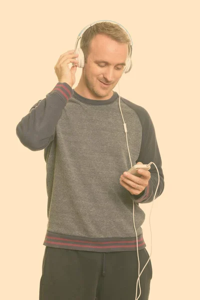 Onnellinen komea valkoihoinen mies kuuntelee musiikkia ja käyttää matkapuhelinta — kuvapankkivalokuva
