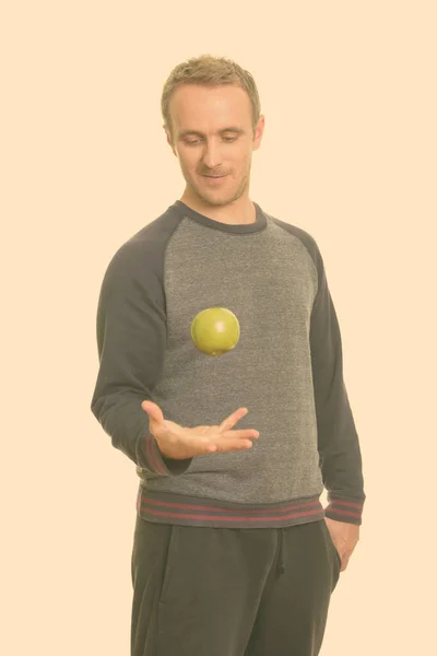 Retrato de un hombre guapo con el pelo rubio lanzando manzana en el aire — Foto de Stock