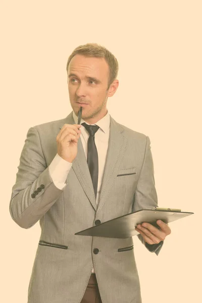 Handsome Caucasian businessman holding pen and clipboard while thinking — Stock Photo, Image