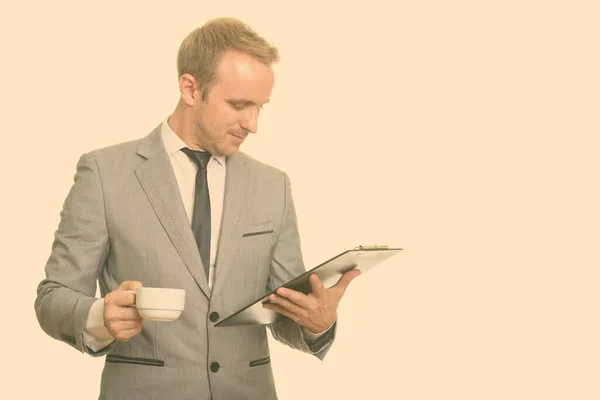 Guapo caucásico hombre de negocios leyendo portapapeles mientras bebe café — Foto de Stock