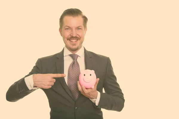 Junger glücklicher kaukasischer Geschäftsmann hält Sparschwein und zeigt mit dem Finger — Stockfoto