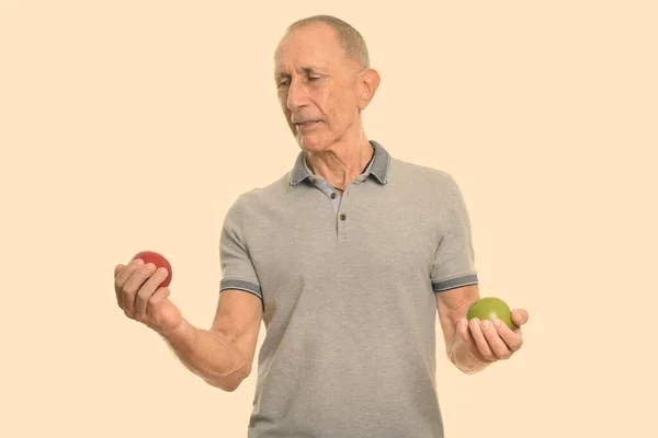 Студийный снимок пожилого человека, смотрящего на красное яблоко, держа зеленое яблоко — стоковое фото