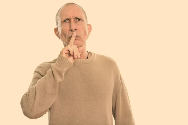 Studio shot van boze senior man met vinger op de lippen — Stockfoto