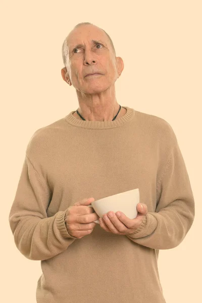 Студийный снимок пожилого человека, держащего чашку кофе, думая — стоковое фото