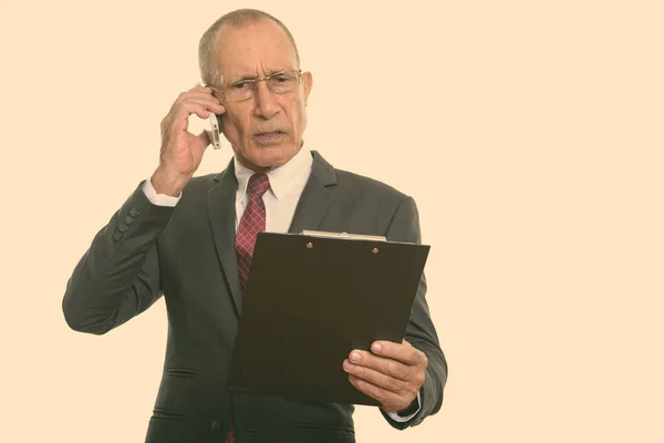 Studioaufnahme eines leitenden Geschäftsmannes, der auf Klemmbrett liest, während er mit dem Handy spricht — Stockfoto