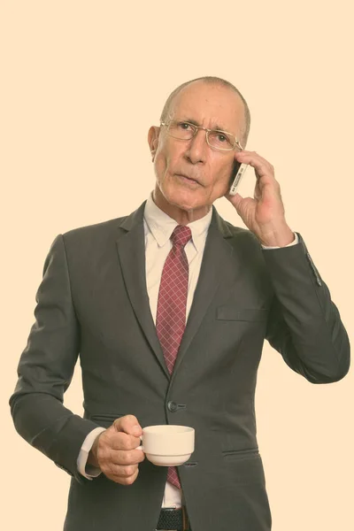 Студийный снимок старшего бизнесмена, держащего чашку кофе во время разговора по мобильному телефону — стоковое фото