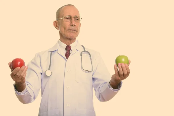 Estudio de tiro de hombre mayor médico sosteniendo manzana roja y mirando a la manzana verde —  Fotos de Stock