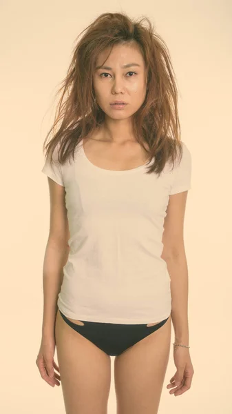Beyaz gömlekli, pantolonsuz ve beyaz arka planda dağınık saçlı genç Asyalı kadının stüdyo fotoğrafı. — Stok fotoğraf