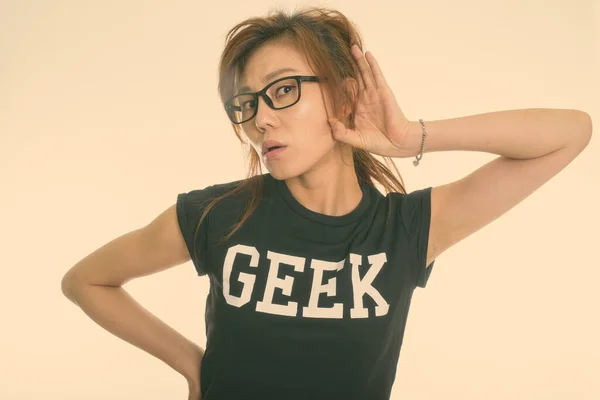 Studio skott av ung asiatisk nörd flicka lyssnar när du bär glasögon mot vit bakgrund — Stockfoto
