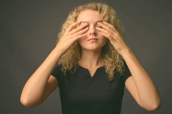 Ung vacker kvinna med lockigt blont hår mot grå bakgrund — Stockfoto