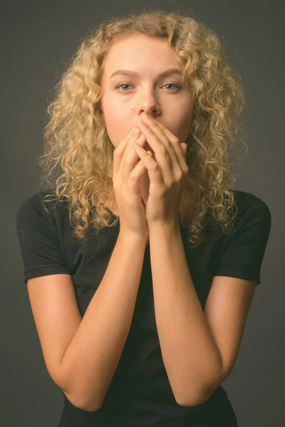 Mladá krásná žena s kudrnaté blond vlasy proti šedému pozadí — Stock fotografie