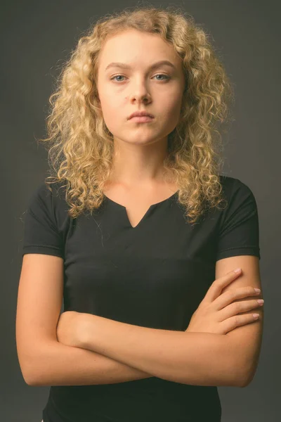 Junge schöne Frau mit lockigen blonden Haaren vor grauem Hintergrund — Stockfoto