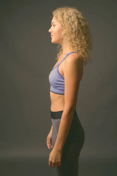 Jovem mulher bonita com cabelo louro encaracolado pronto para ginásio contra fundo cinza — Fotografia de Stock
