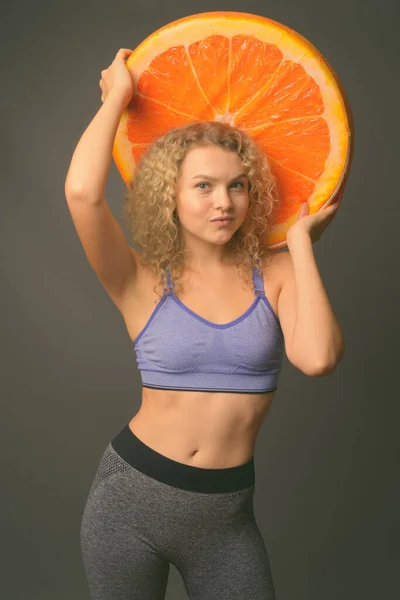 Young beautiful woman with curly blond hair ready for gym against gray background — Stock Photo, Image