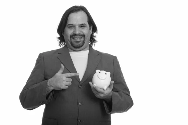 Glücklicher fetter kaukasischer Geschäftsmann lächelt und hält Sparschwein, während er mit dem Finger zeigt — Stockfoto