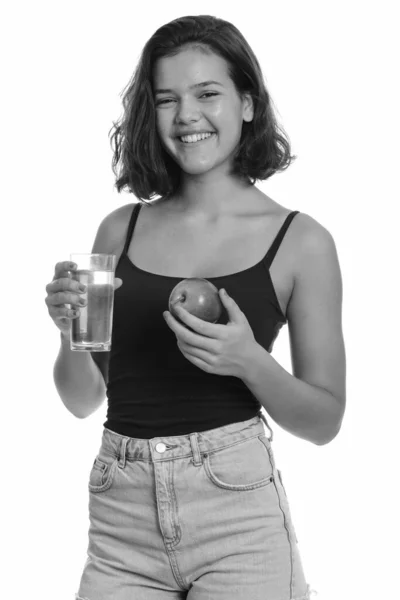 Νεαρή ευτυχισμένη Καυκάσια έφηβη χαμογελά κρατώντας ένα ποτήρι νερό και μήλο — Φωτογραφία Αρχείου