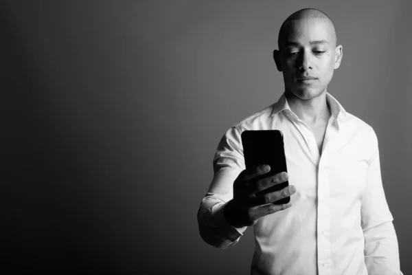 Handsome bald businessman using mobile phone against gray background