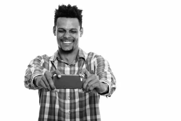 Studio skott av ung glad afrikansk man ler när du tar bild med mobiltelefon — Stockfoto