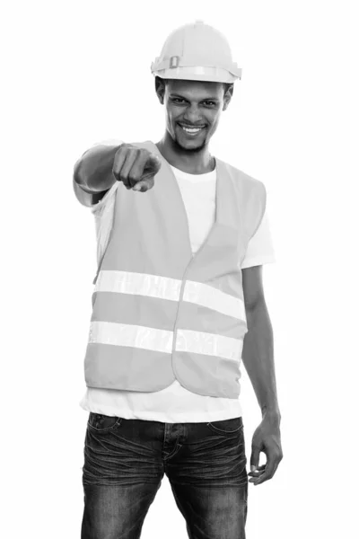 Młody szczęśliwy Afrykanin budowlany pracownik uśmiecha się a wskazując na aparat — Zdjęcie stockowe