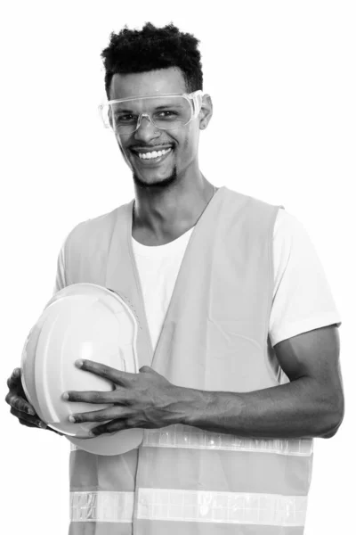 Zamyšlený šťastný africký muž stavební dělník s úsměvem při držení bezpečnostní přilbu — Stock fotografie
