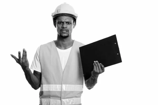 Joven hombre africano enojado trabajador de la construcción sosteniendo portapapeles con ambos brazos levantados —  Fotos de Stock