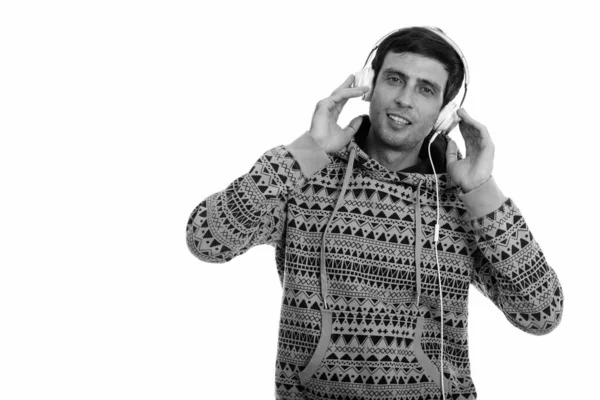 Студийный снимок молодого счастливого человека, улыбающегося и слушающего музыку, держа наушники — стоковое фото