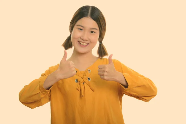 젊고 행복 한 아시아 여성 이 엄지손가락을 내밀면서 웃고 있는 스튜디오 촬영 — 스톡 사진